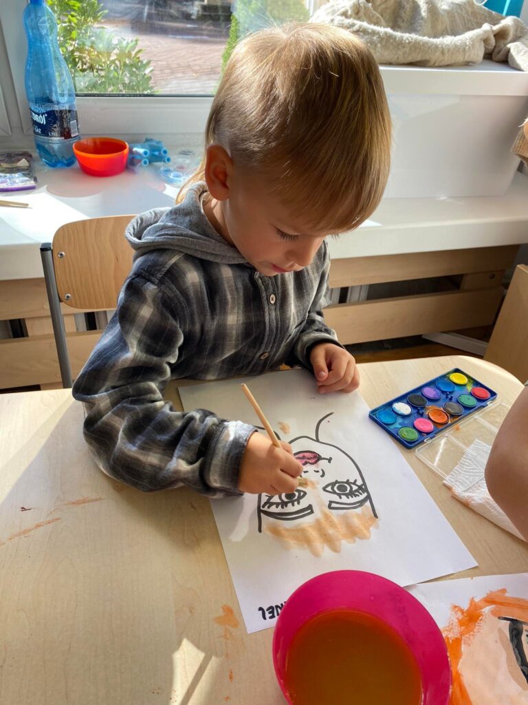 Chłopiec maluje farbami wodnymi Panią Jesień.