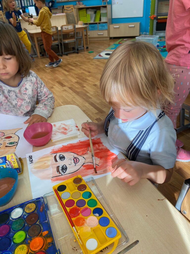 Dziewczynka i chłopiec siedząc przy stoliku malują farbami akwarelowymi.