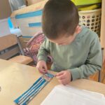 Chłopiec przykleja ścinki z kredek do swojej pracy.