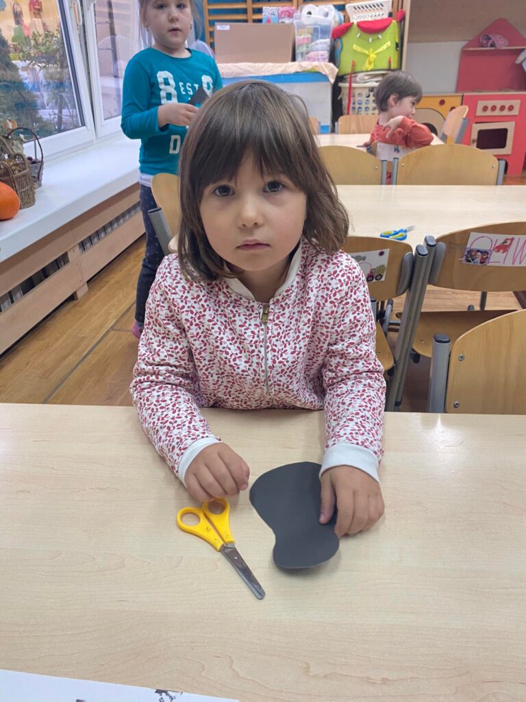 Przedszkolak siedząc przy stoliku wycina kształt sroki.