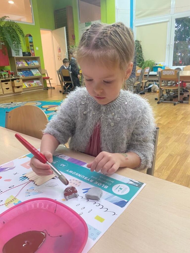 Dziecko z grupy "Słoneczka" maluje farbą renifera z gliny.