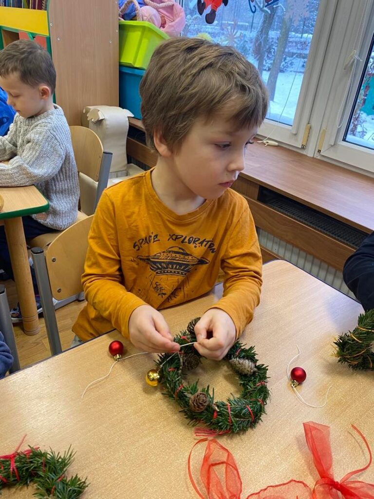 Dziecko z grupy "Słoneczka" wykonuje świąteczny wianek podczas warsztatów.