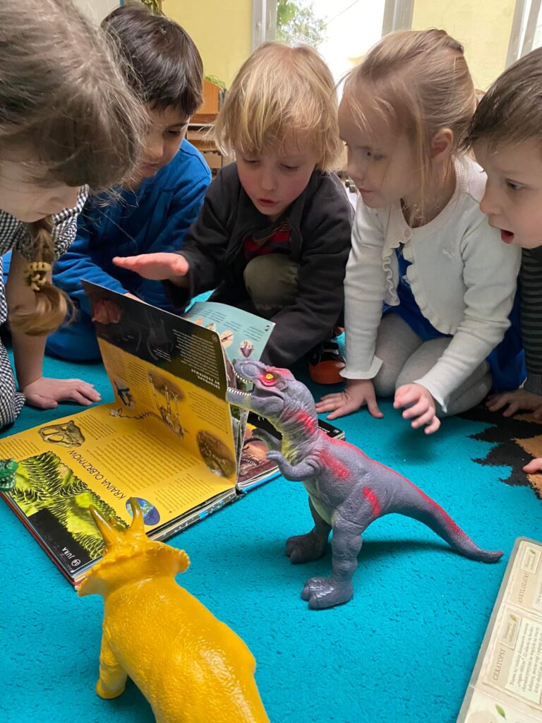 Dzieci oglądają książkę o dinozaurach.