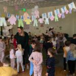 Dzieci ubrane w piżamy tańczą w przystrojonej sali.
