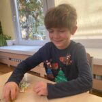 Chłopiec siedząc przy stoliku układa wzór z koralików.