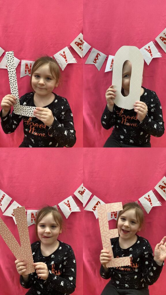Dziecko pozuje do czterech zdjęć z literami składającymi się na napis "LOVE".