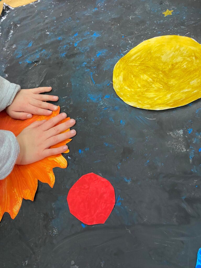 Dziecko przykleja wykonane z papieru słońce do grupowego plakatu.