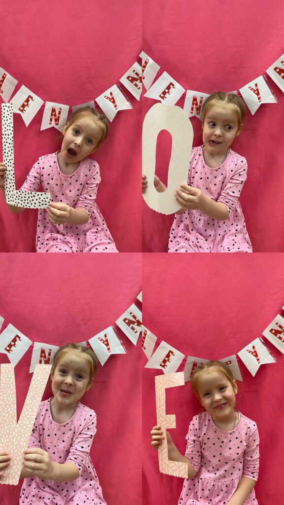 Dziecko pozuje do czterech zdjęć z literami składającymi się na napis "LOVE".