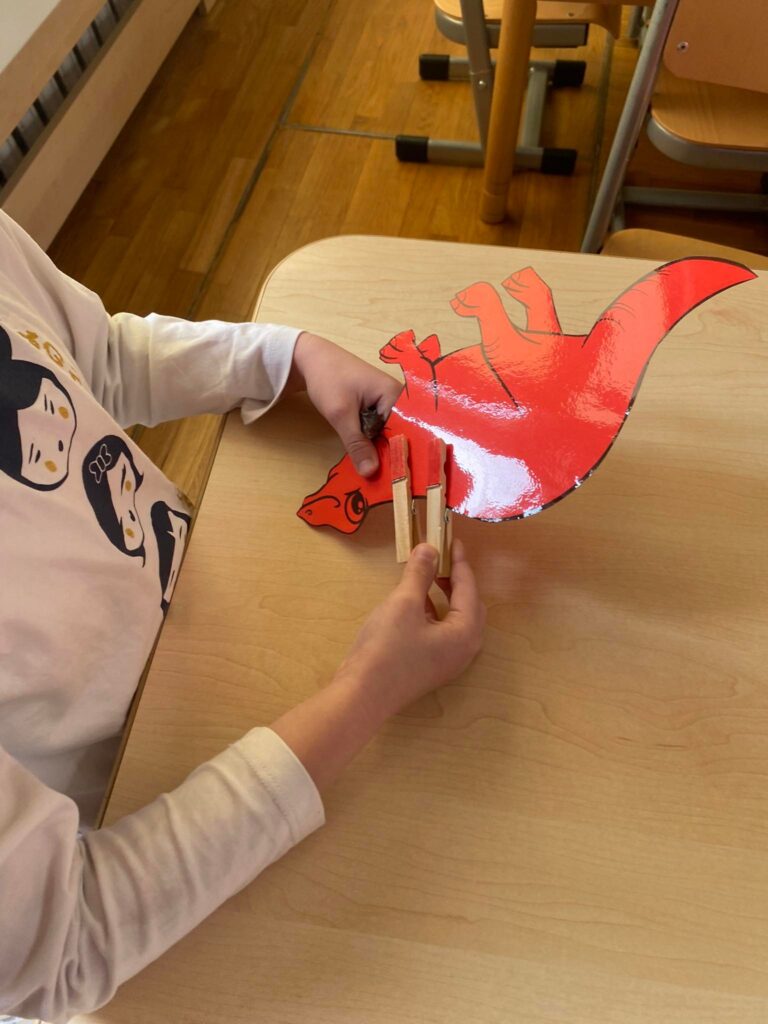 Dziecko przypina spinacze do papierowego dinozaura.
