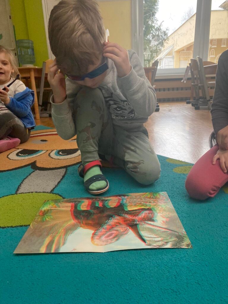 Dzieci oglądają obrazki przedstawiające dinozaury w okularach 3d.