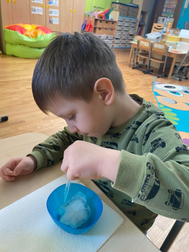 Chłopiec siedząc przy stoliku rozpuszcza bryły lodu za pomocą pipety.