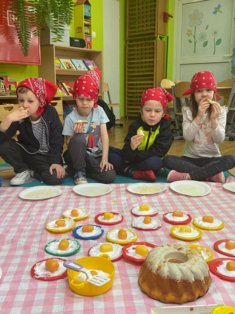 Dzieci siedząc na dywanie jedzą kanapki z pastą jajeczną przygotowaną podczas zajęć.