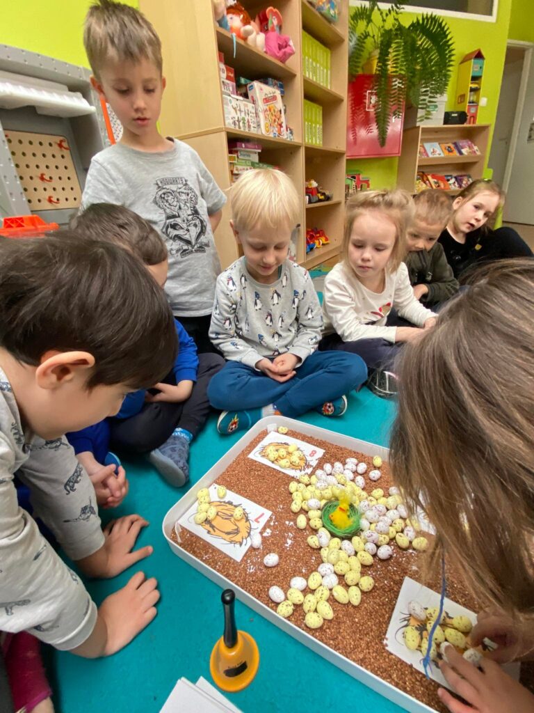 Dzieci liczą jajka na przygotowanej planszy z gniazdami.