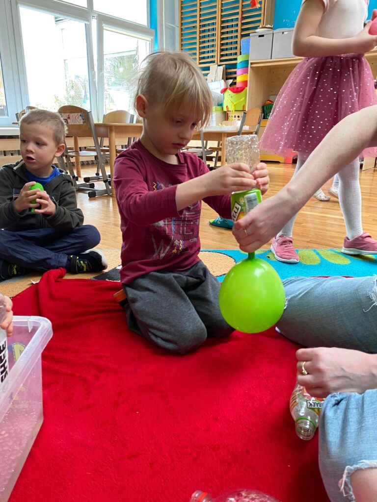 Dzieci siedząc na dywanie wykonują gniotki z kulek i balonów.