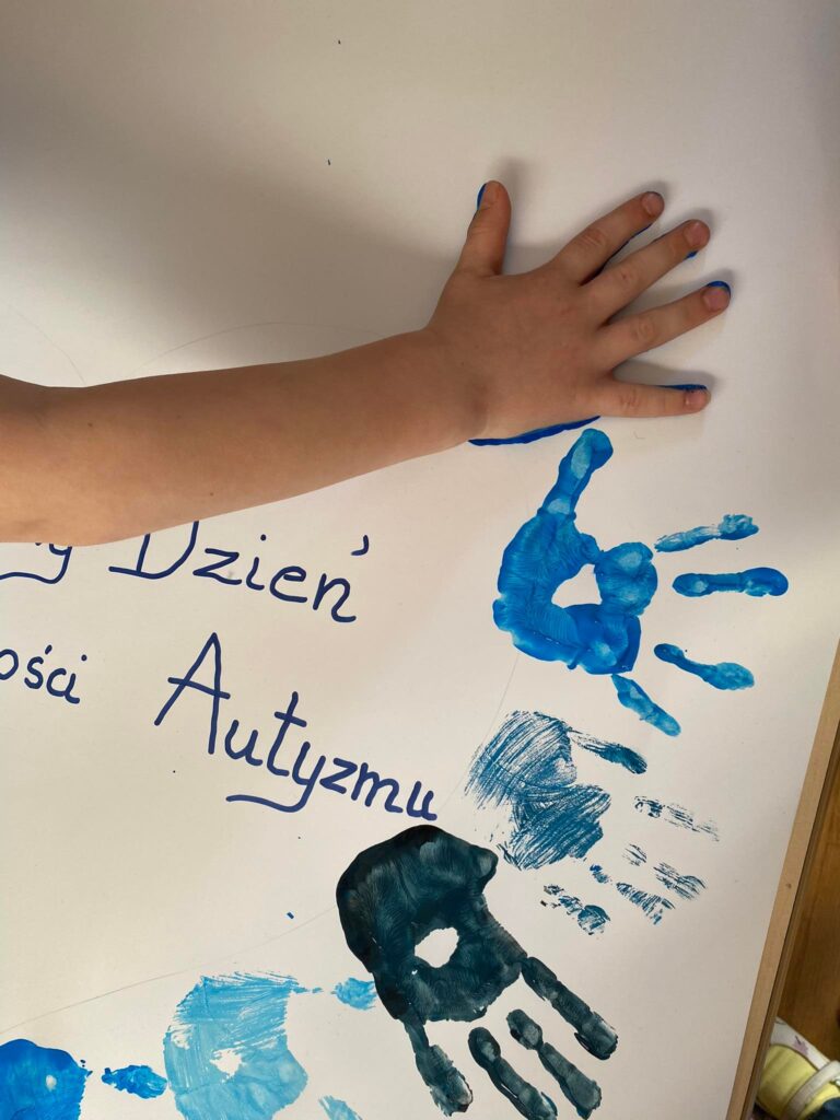 Dziecko odbija rękę umalowaną niebieską farbą.