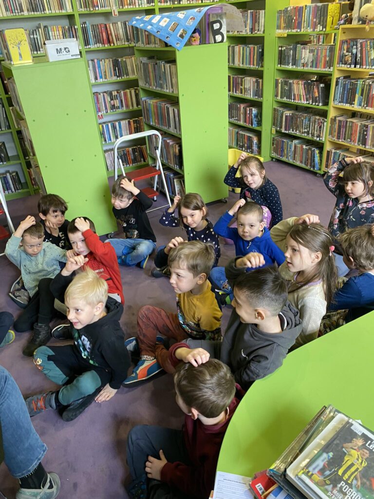 Dzieci siedząc na dywanie biorą udział w warsztatach bibliotecznych.
