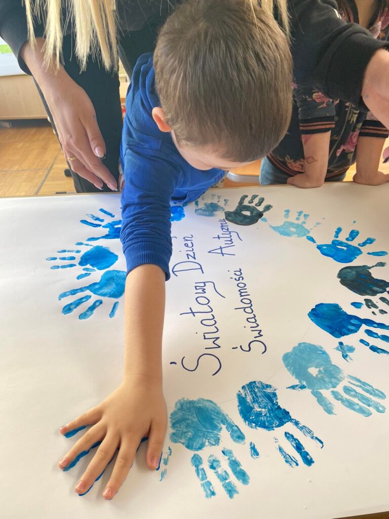 Dziecko odbija rękę umalowaną niebieską farbą.