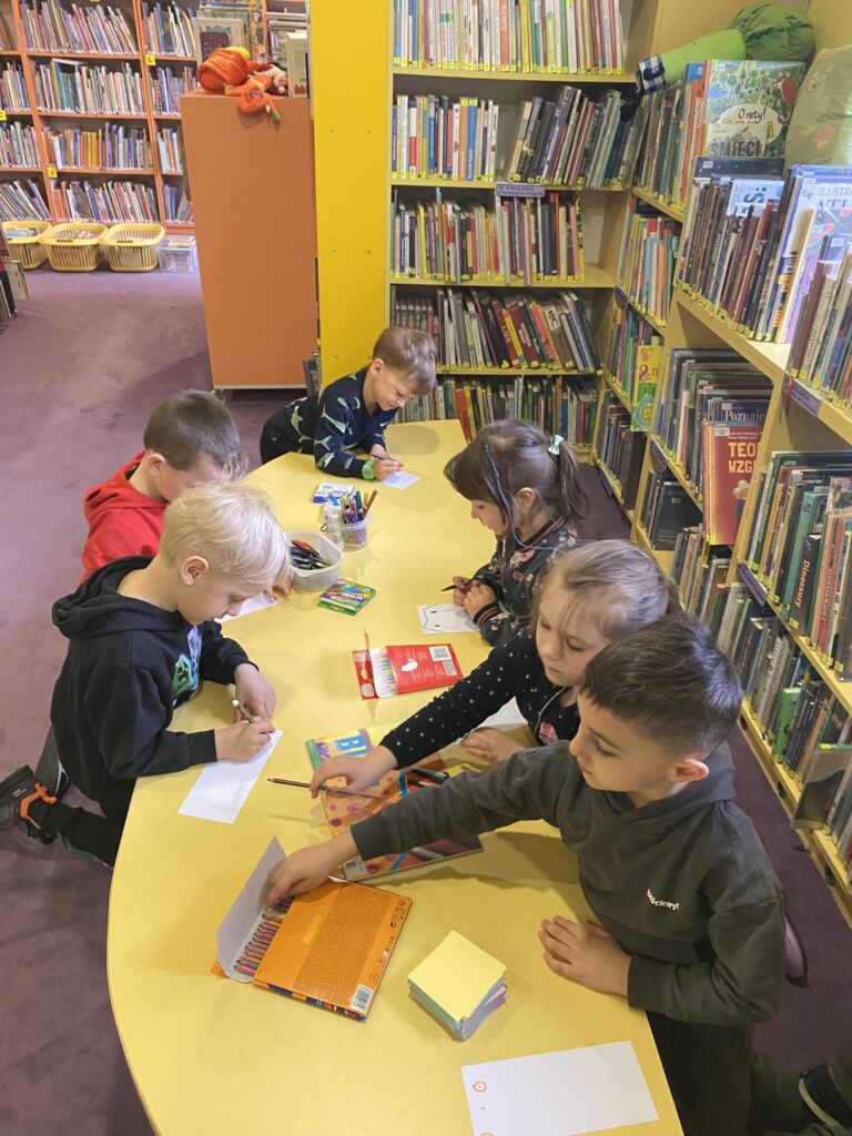 Dzieci wykonują papierowe mole książkowe podczas zajęć w bibliotece.