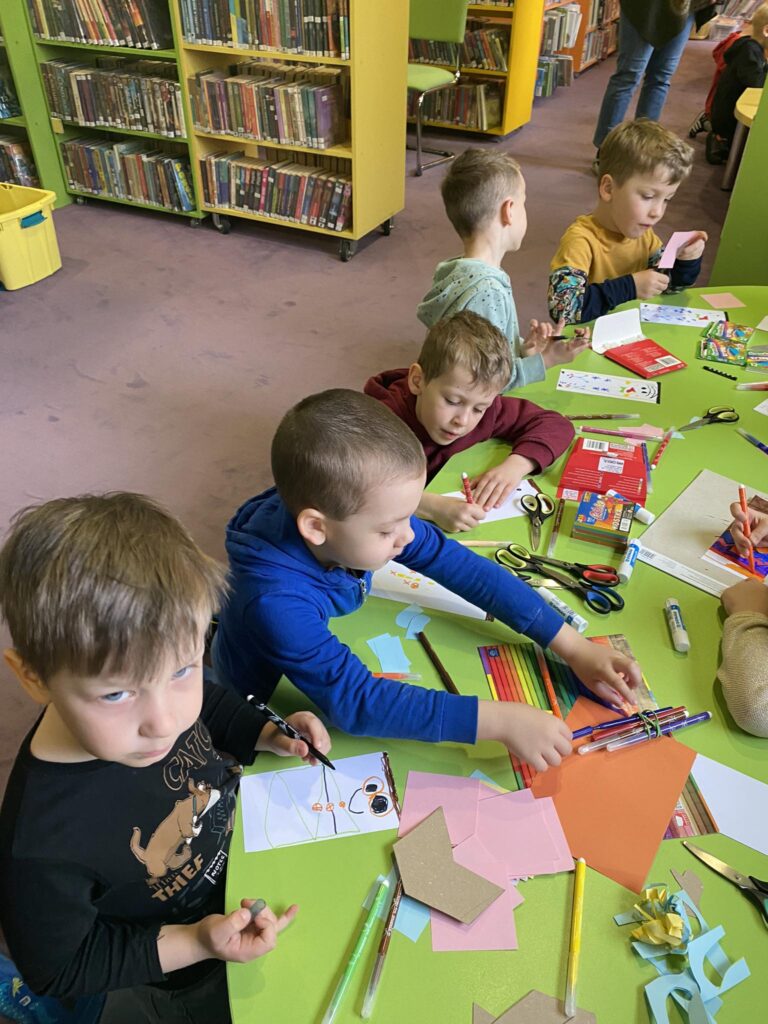 Dzieci wykonują papierowe mole książkowe podczas zajęć w bibliotece.