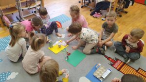Dzieci układające różne opakowania na odpowiednich kolorach (segregujące odpady)