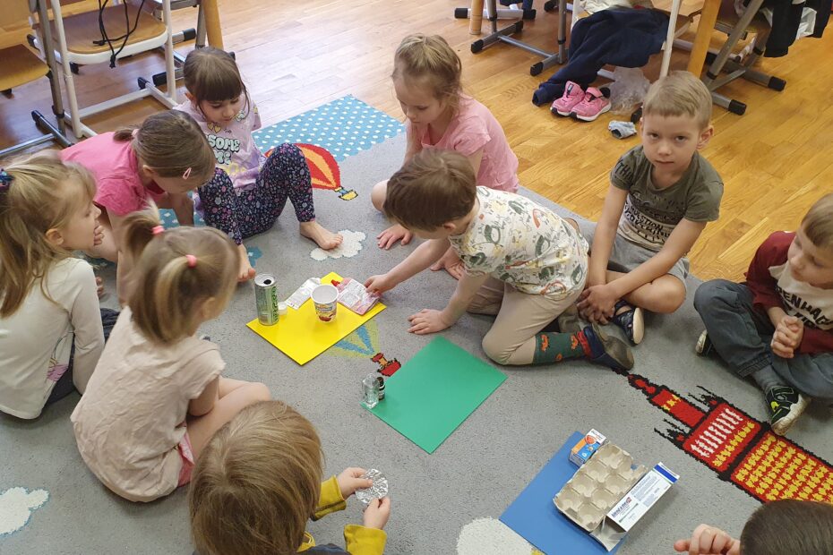 Dzieci układające różne opakowania na odpowiednich kolorach (segregujące odpady)